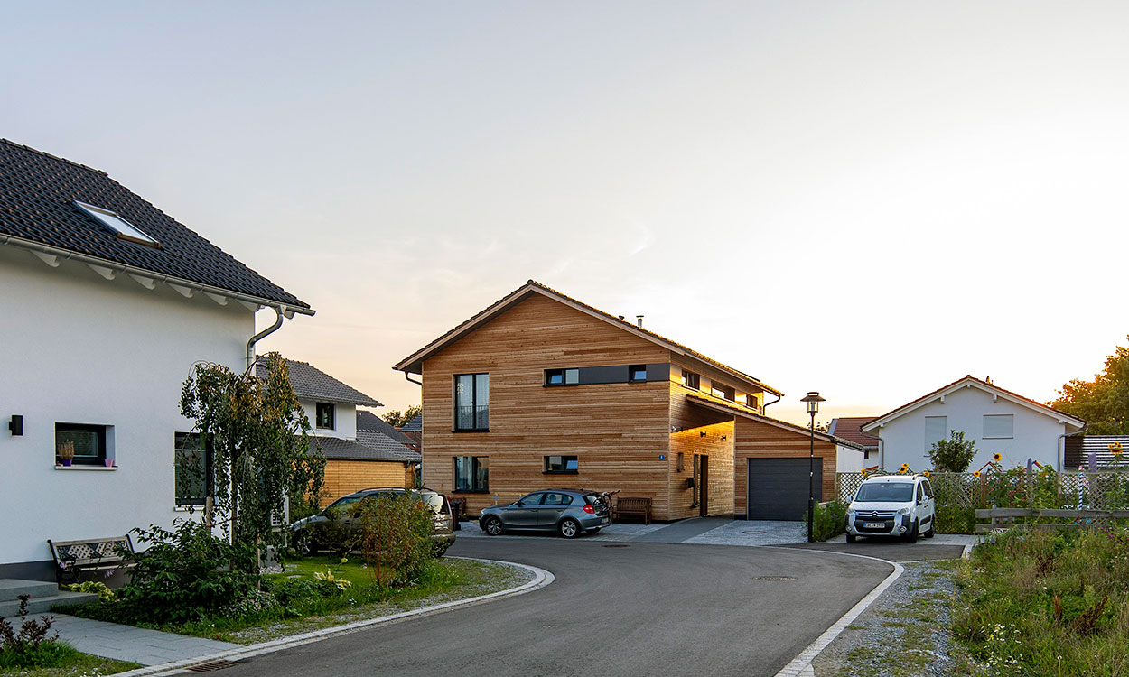 Ein modernes Holzhaus in Oberpframmern leuchtet bei Sonnenuntergang in einer ruhigen Wohnsiedlung.