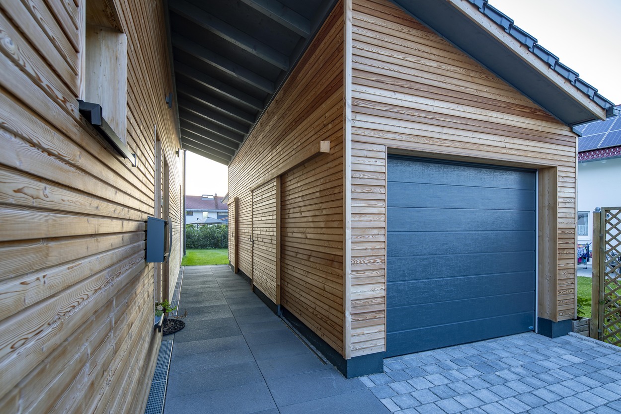 Ein modernes Holzhaus in Oberpframmern zeigt klare Linien, eine blaue Garagentür und einen gepflegten Außenbereich.