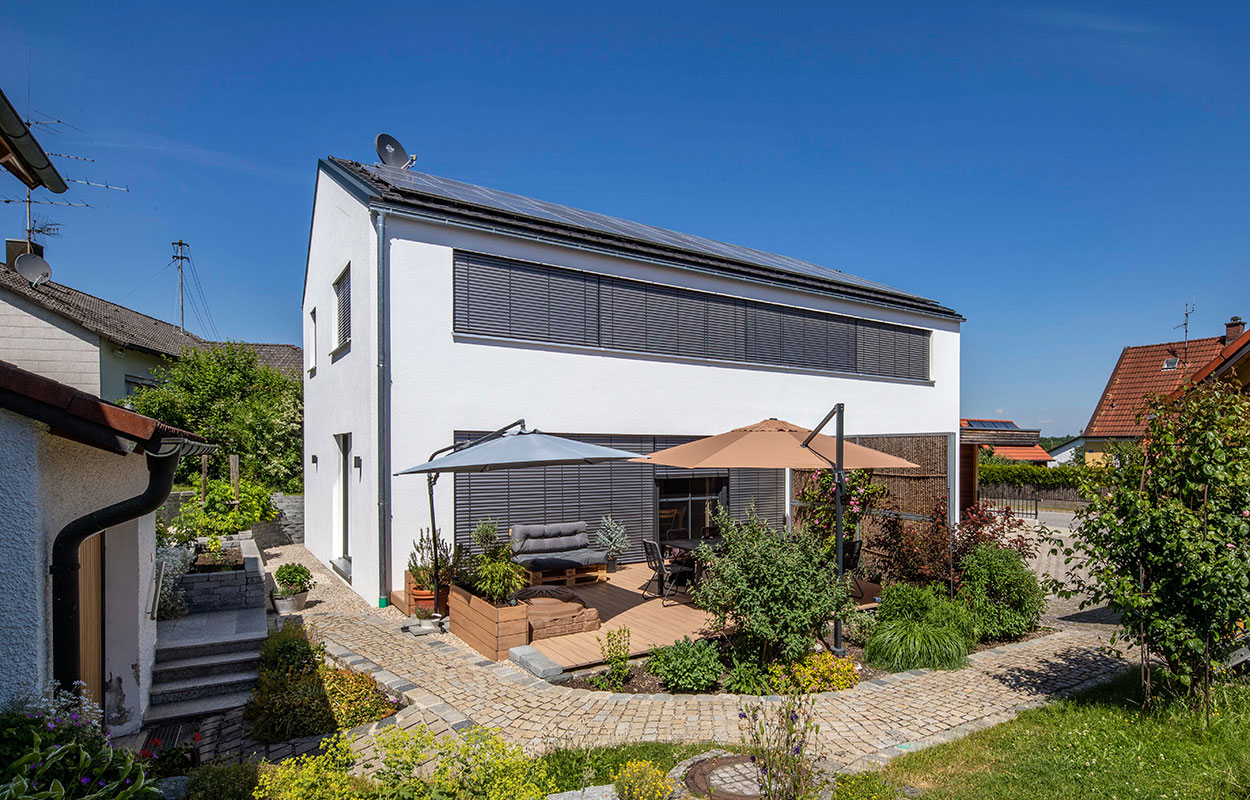 Ein modernes Passivhaus in Fahrenzhausen mit Solarpanelen und gemütlicher Terrasse, umgeben von einem üppigen Garten.