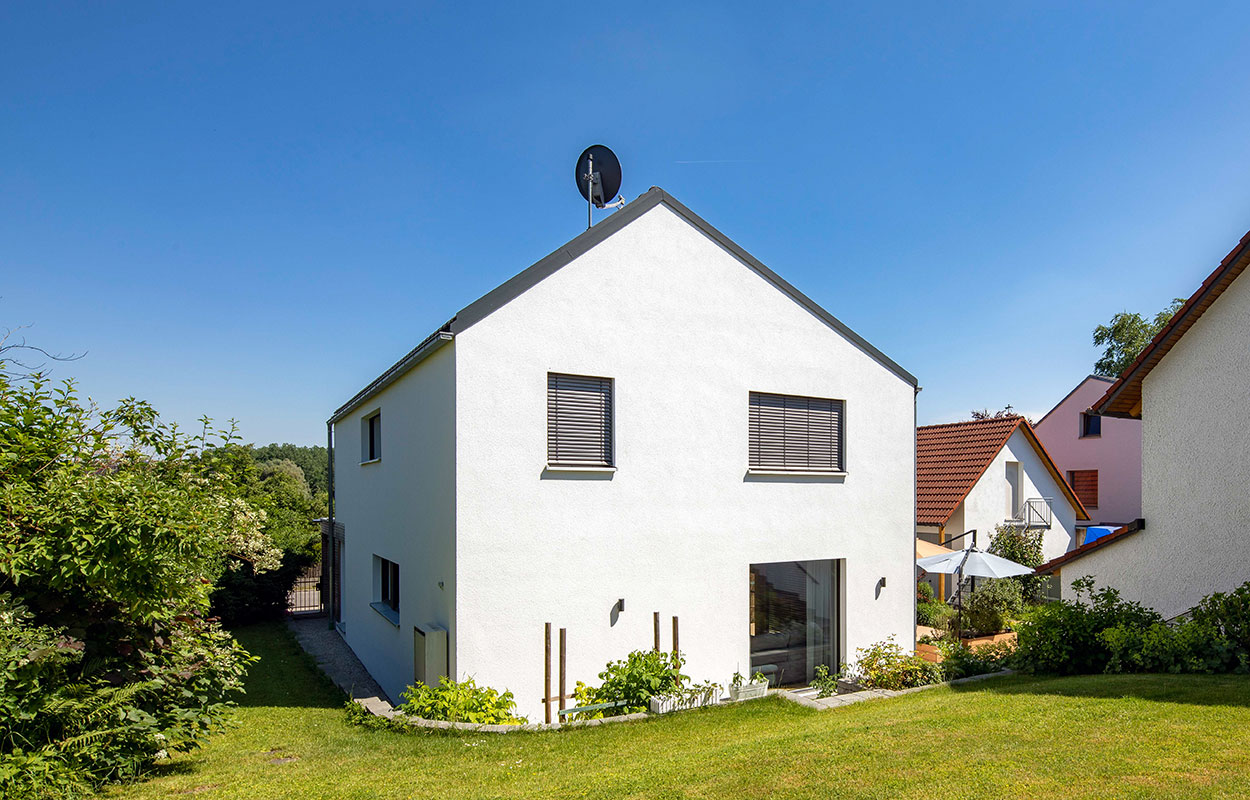 Ein modernes Passivhaus in Fahrenzhausen steht unter klarem Himmel, umgeben von einem gepflegten Garten.