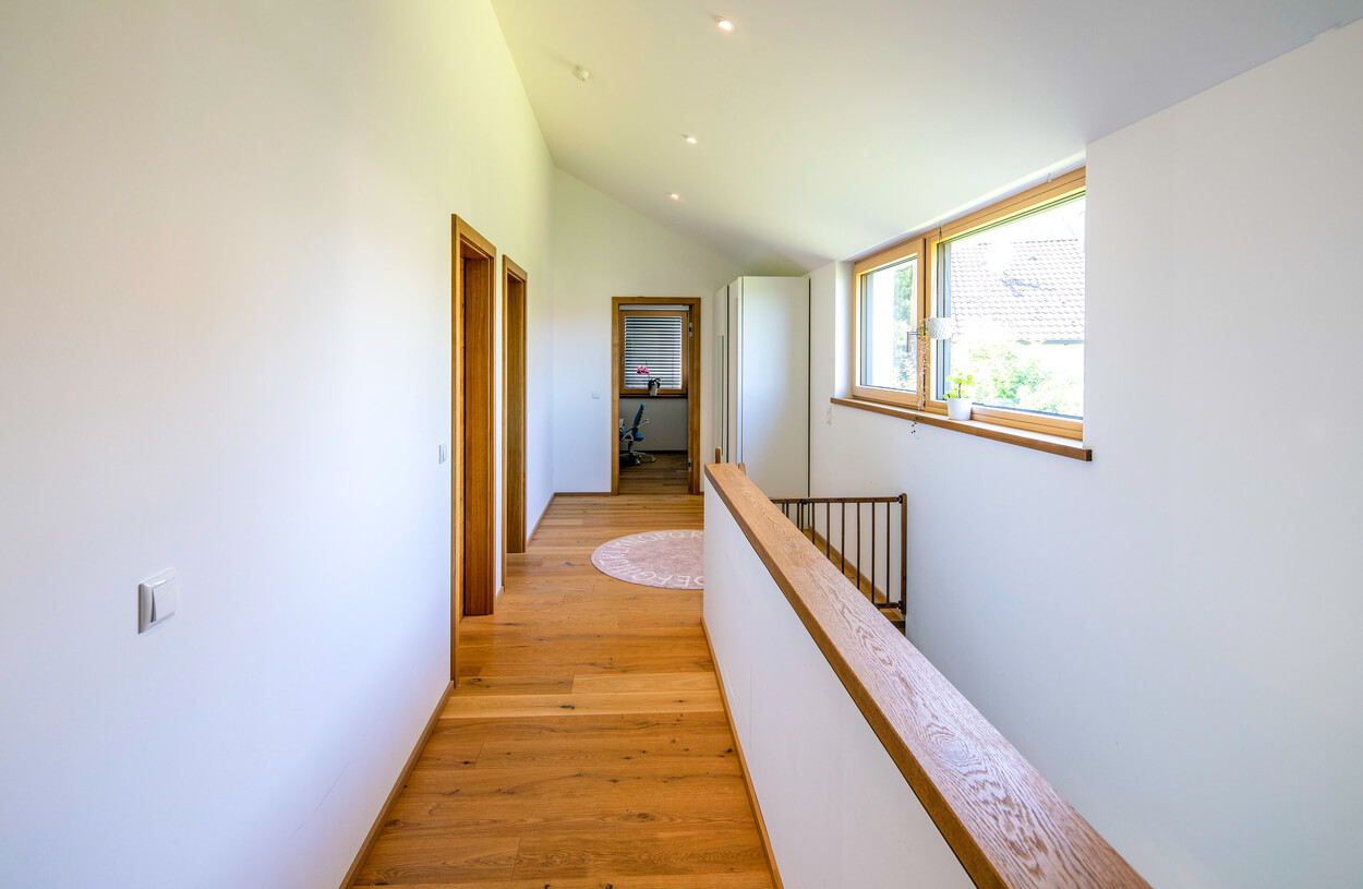 Ein heller Flur in einem Passivhaus in Fahrenzhausen zeigt Holzfußboden und große Fenster, die viel Tageslicht hereinlassen.