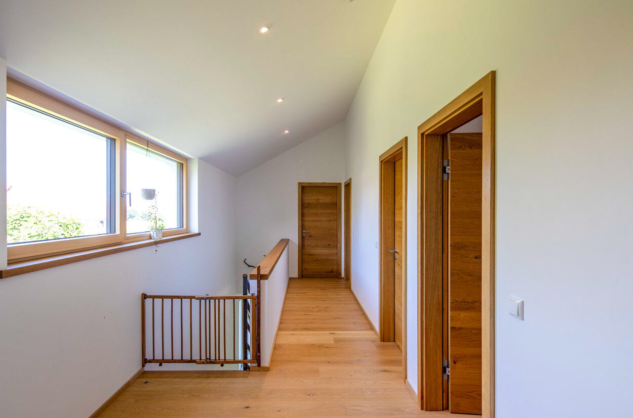 Ein heller Flur im Passivhaus Fahrenzhausen zeigt Holztüren und große Fenster, die viel natürliches Licht einlassen.