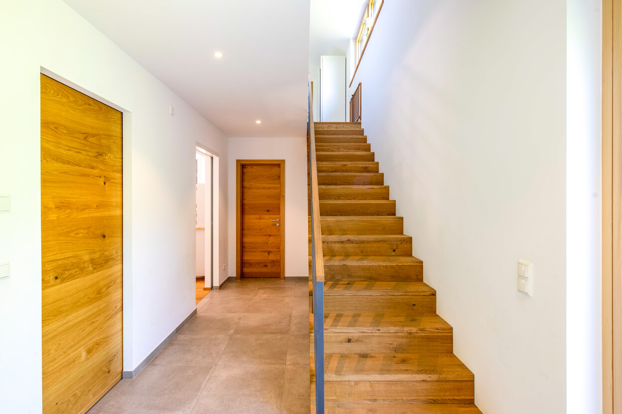 Ein moderner Flur in einem Passivhaus in Fahrenzhausen zeigt eine elegante Holztreppe und warme Holztüren.