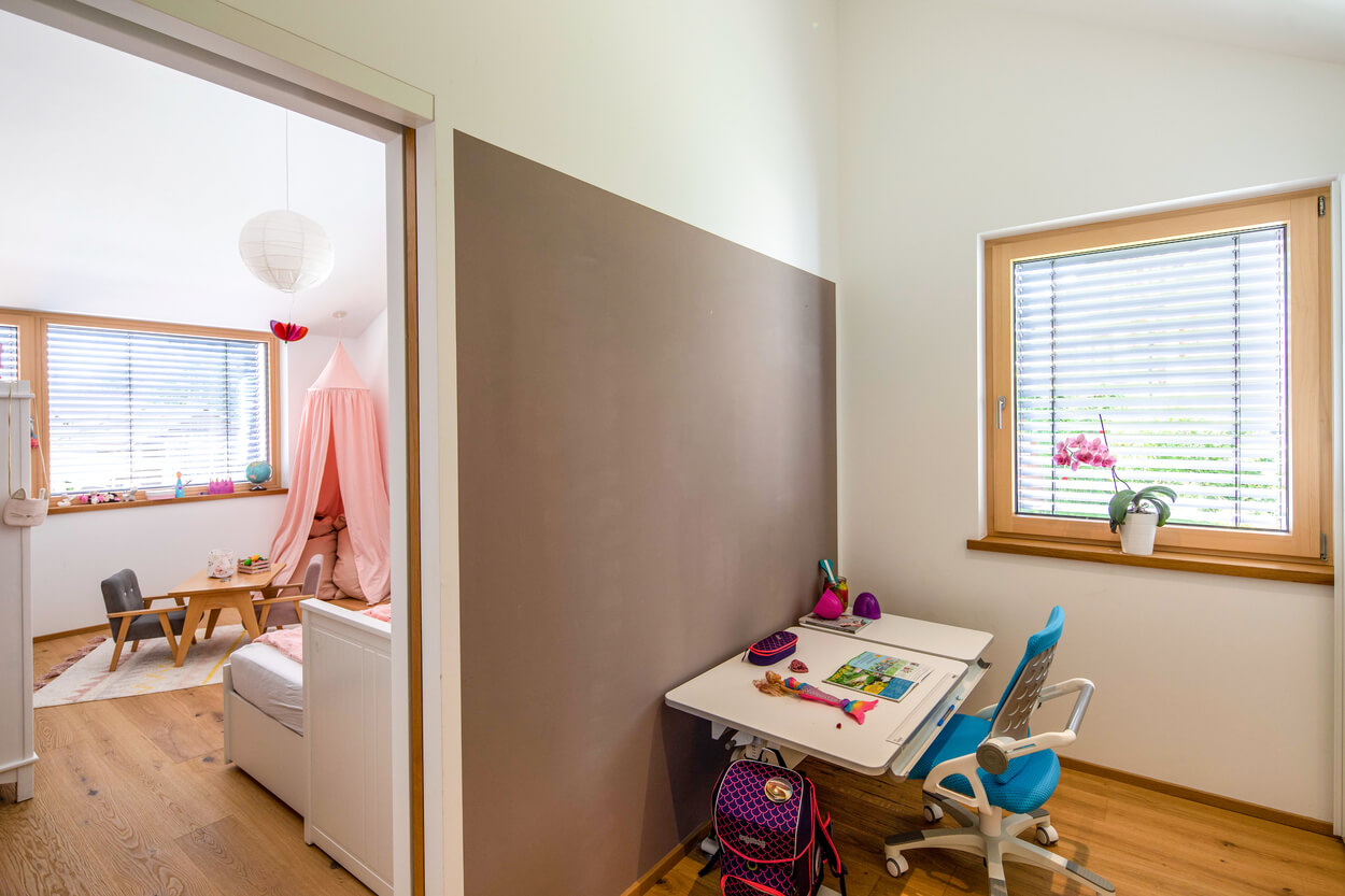 Ein modernes Kinderzimmer in Fahrenzhausen zeigt einen Spielbereich und einen Schreibtisch am Fenster im Passivhaus.