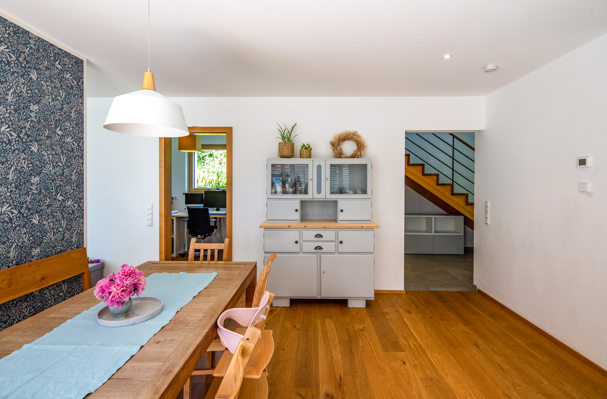 Der Wohnbereich eines Passivhauses in Fahrenzhausen zeigt einen Esstisch mit Blumen und eine moderne Treppe im Hintergrund.