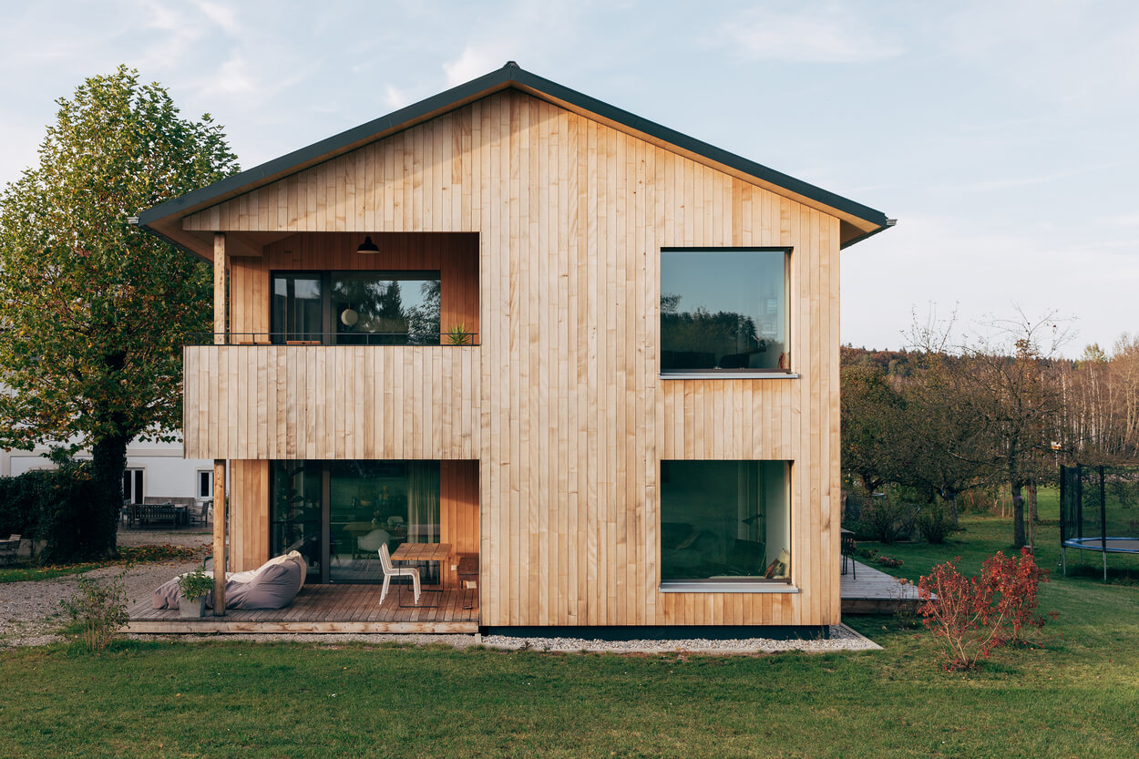Ein modernes Holzhaus mit großen Fenstern steht idyllisch in der grünen Landschaft des Chiemgaus, perfekt als Ferienhaus.