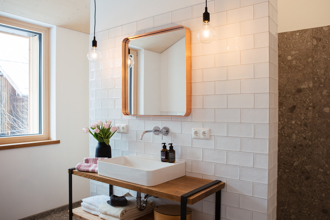 Ein stilvolles Badezimmer im Holzhaus im Chiemgau mit modernem Waschbecken, hölzerner Ablage und dekorativen Tulpen.