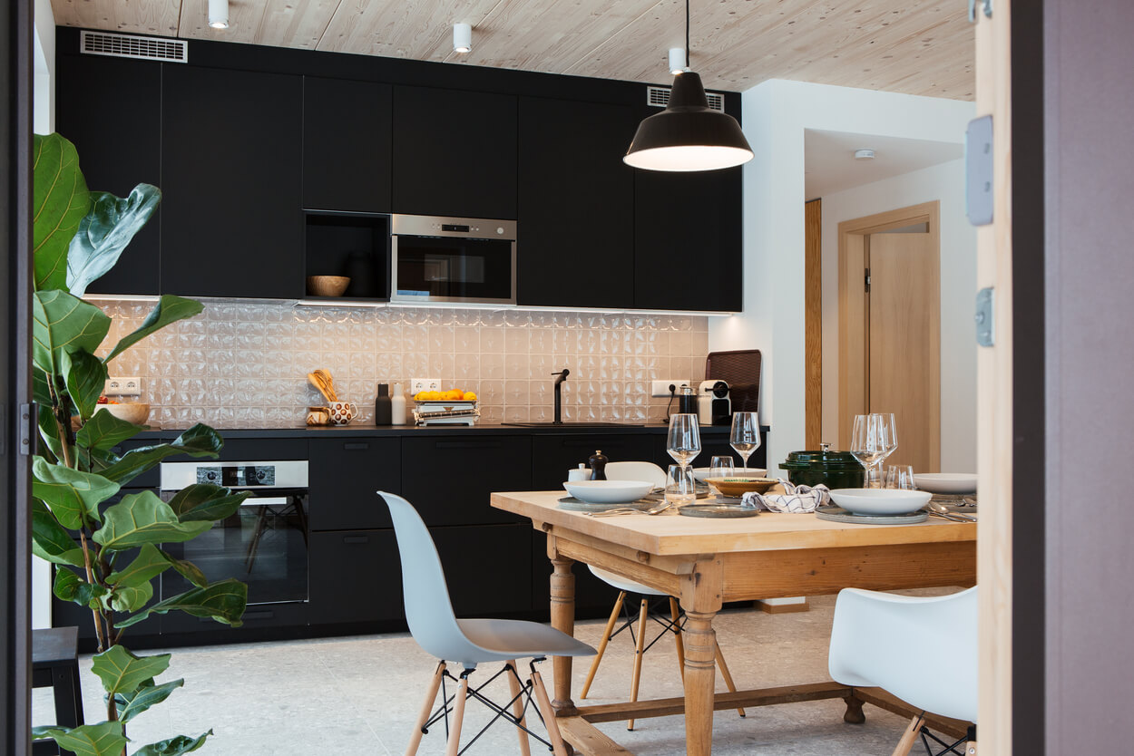 Eine moderne Küche in einem Holzhaus im Chiemgau zeigt einen gedeckten Esstisch vor stilvollen schwarzen Schränken.