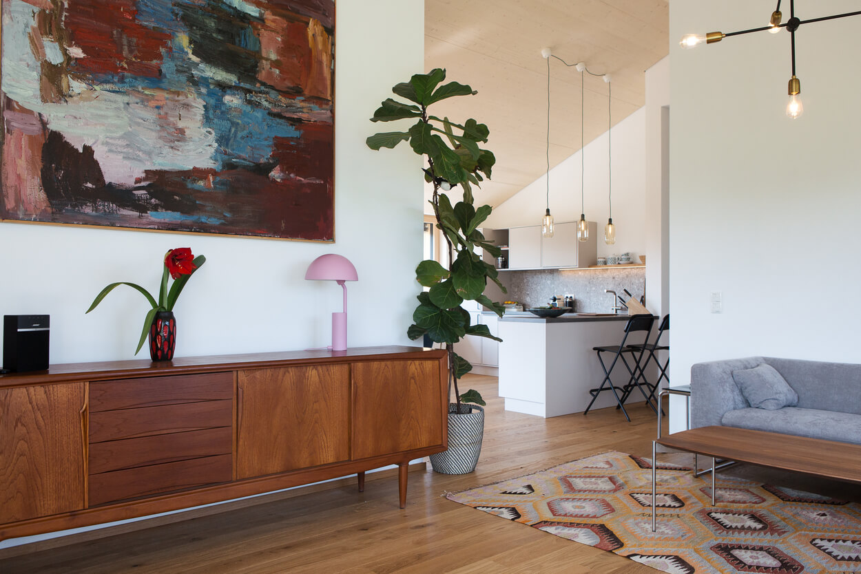 Ein stilvolles Wohnzimmer im Holzhaus Chiemgau mit moderner Einrichtung und großem, buntem Wandgemälde.