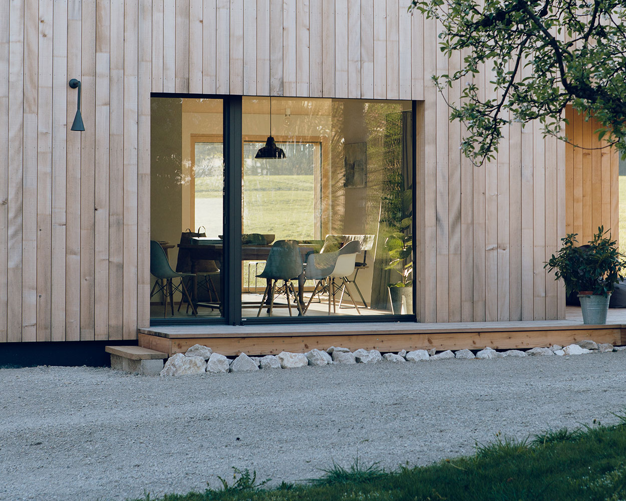 Ein modernes Holzferienhaus im Chiemgau zeigt durch große Fenster einen einladenden Essbereich mit Blick ins Grüne.