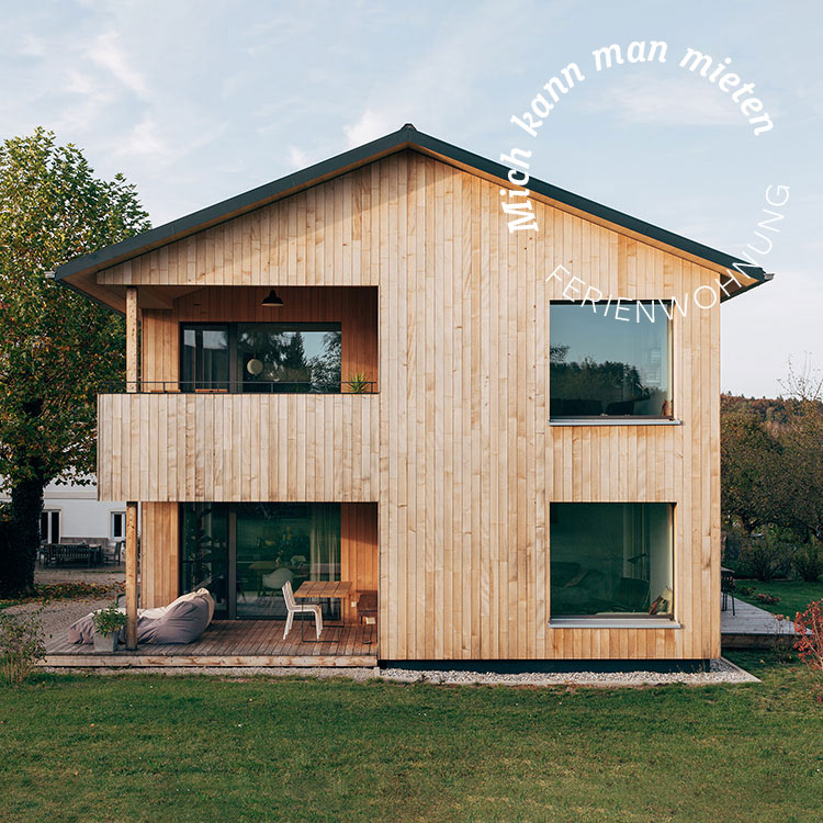 Modernes Holzferienhaus im Chiemgau mit Balkon, umgeben von grüner Natur und einladender Terrasse für entspannte Stunden.