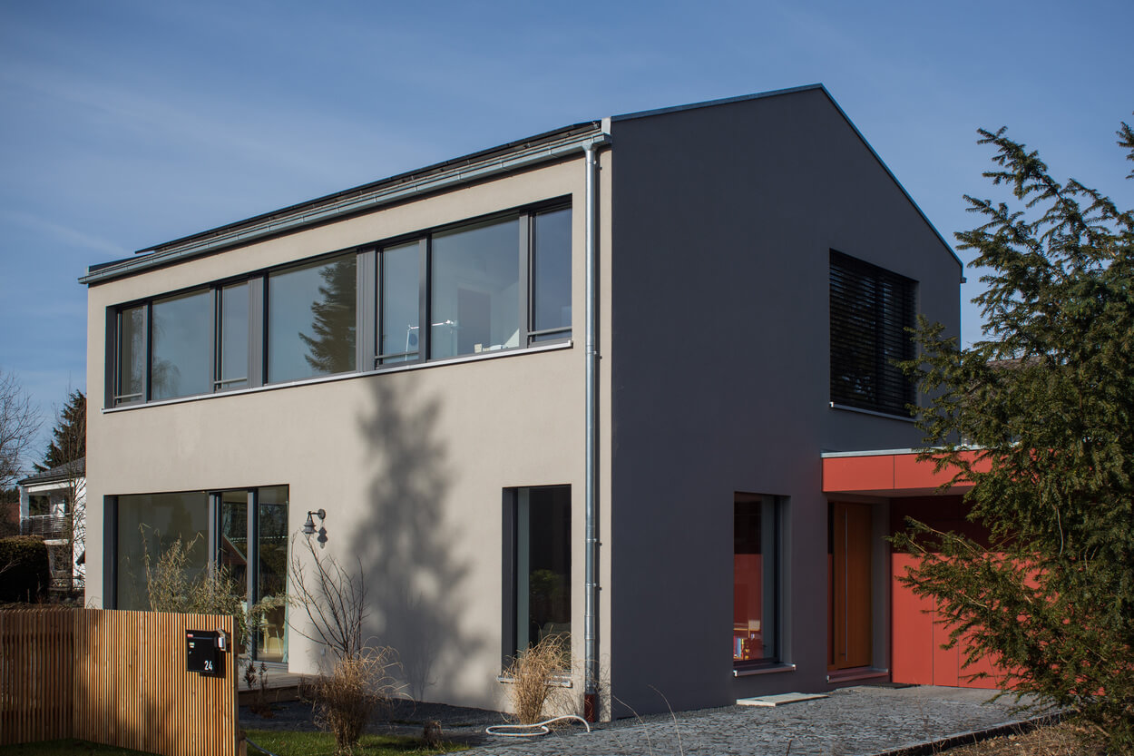 Ein modernes Passivhaus in Baierbrunn zeigt große Fenster und klare Linien unter einem strahlend blauen Himmel.
