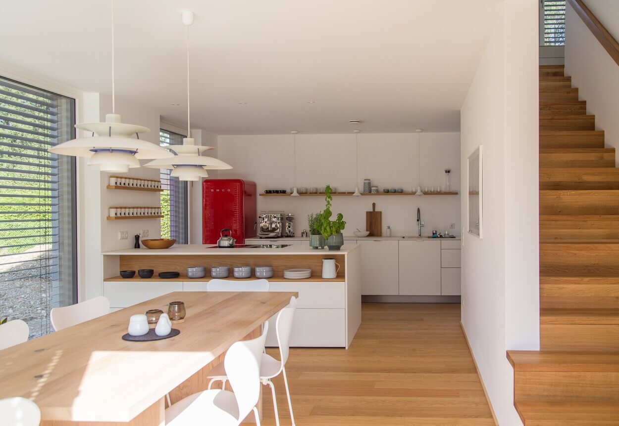 Eine moderne Küche im Passivhaus in Baierbrunn zeigt helles Holzdekor und einen auffälligen roten Kühlschrank.