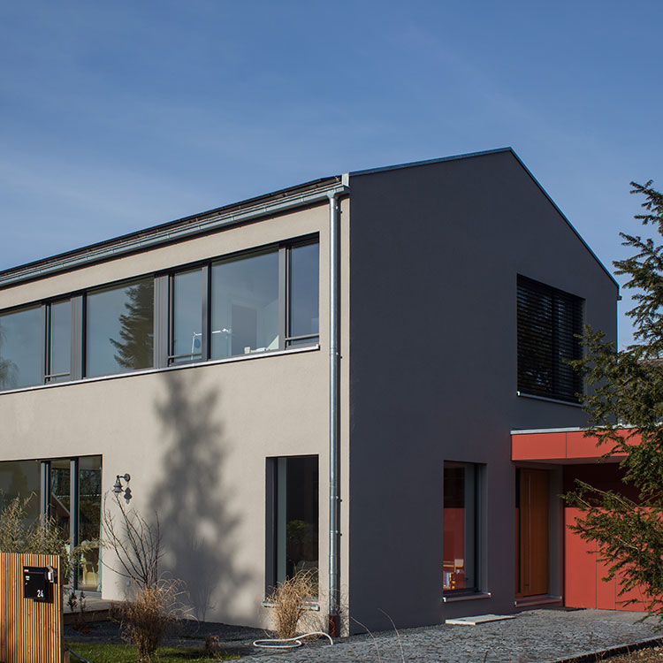 Ein modernes Passivhaus in Baierbrunn mit großen Fenstern und klaren Linien steht unter strahlend blauem Himmel.