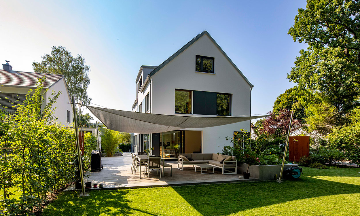 Ein modernes Passivhaus in Eichenau mit schattiger Terrasse und gepflegtem Garten bei sonnigem Wetter.