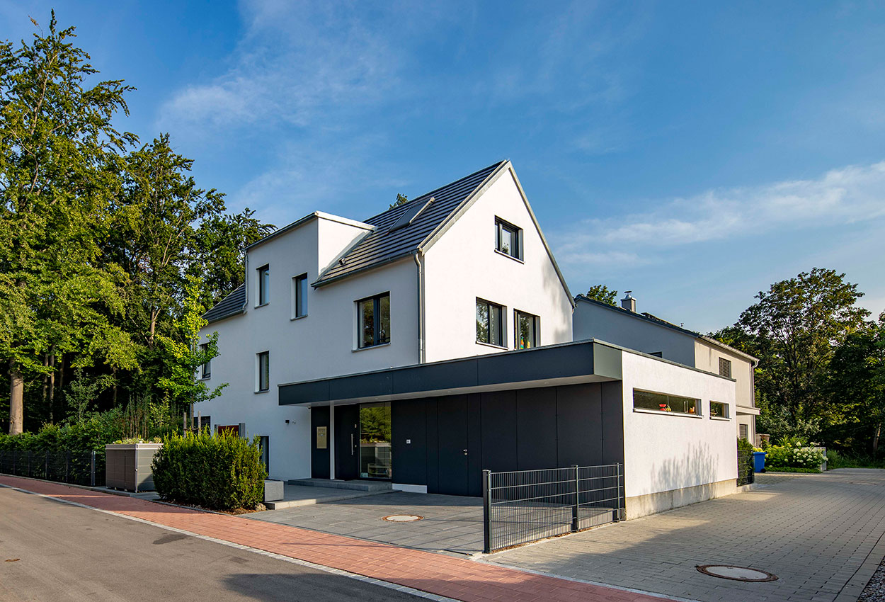 Ein modernes Passivhaus in Eichenau steht unter blauem Himmel, umgeben von üppigen Bäumen.