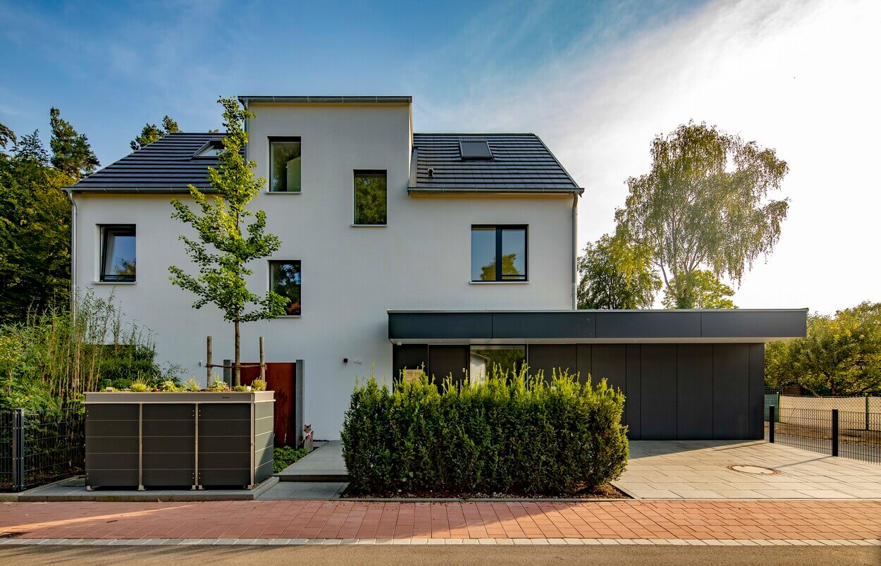 Das moderne Passivhaus in Eichenau steht von grünen Bäumen umgeben unter einem klaren Himmel.
