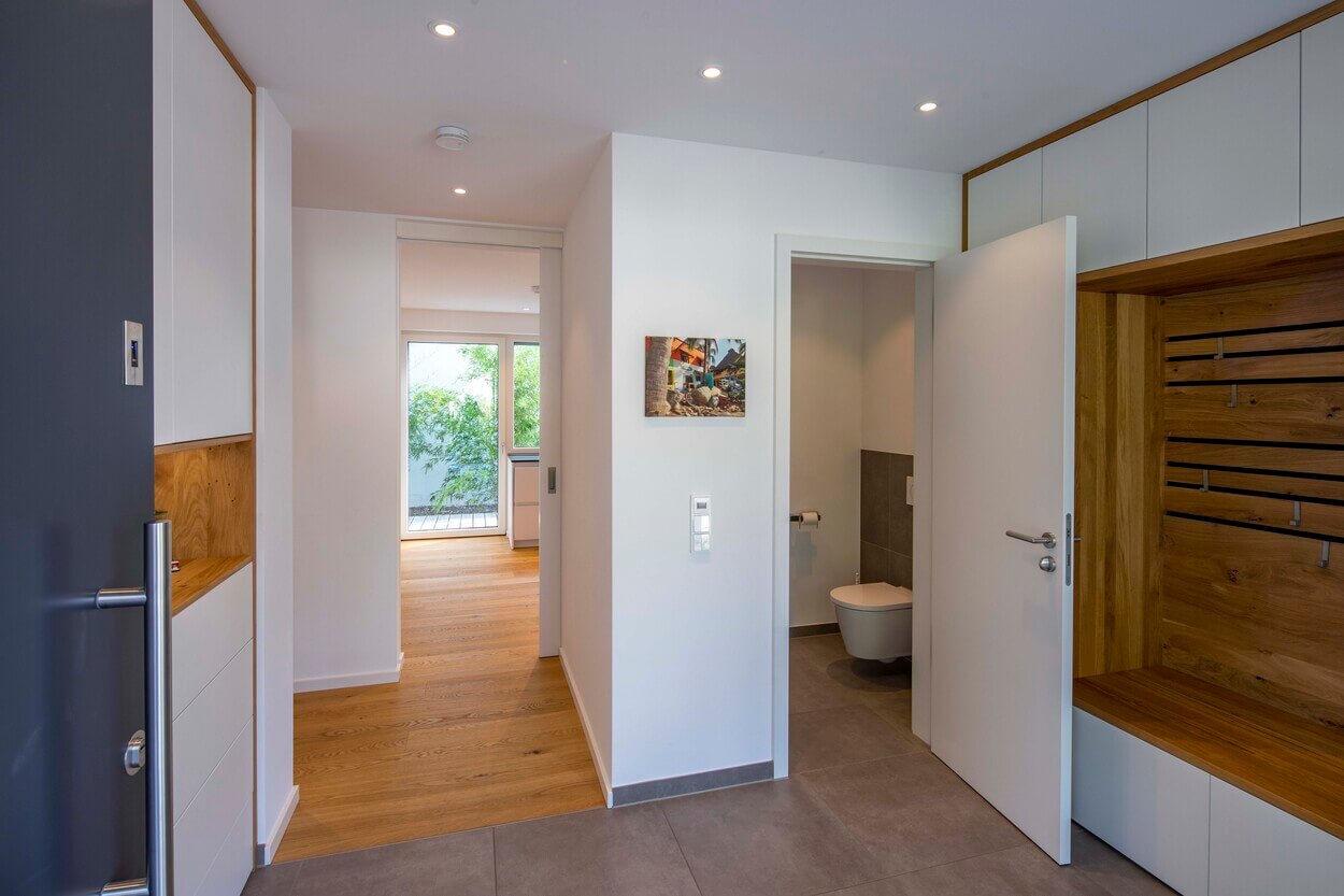Der Eingang des Passivhauses in Eichenau präsentiert helle Holzböden und eine offene Tür zum Badezimmer.