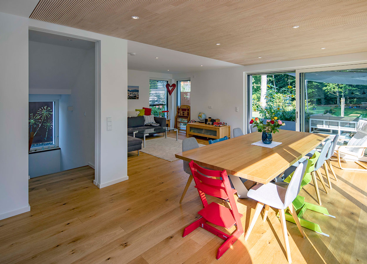 Ein modernes Esszimmer im Passivhaus Eichenau mit Holztisch, bunten Stühlen und Blick auf den sonnigen Garten.