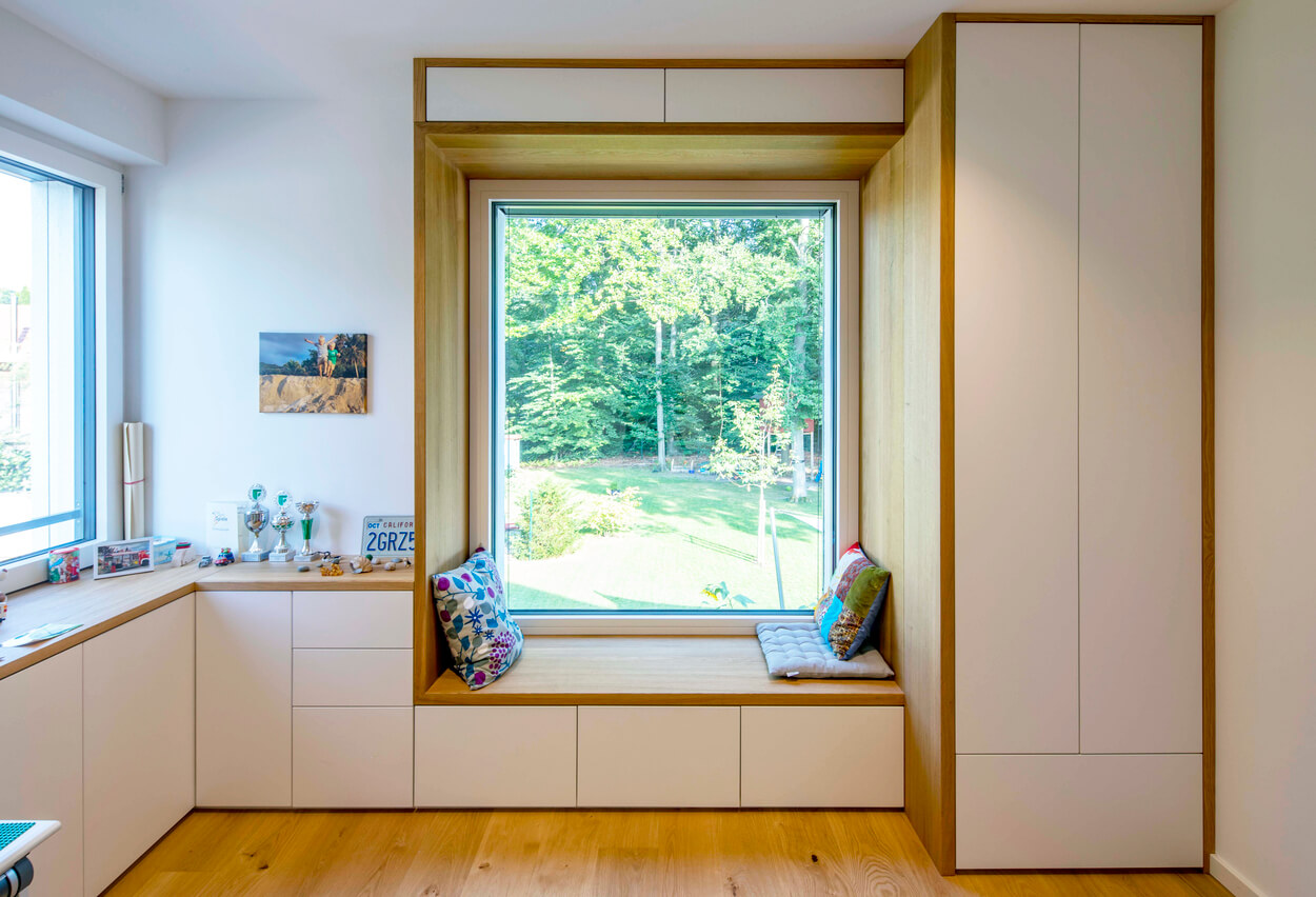 Eine gemütliche Sitzgelegenheit am großen Fenster bietet einen idyllischen Blick ins Grüne in einem modernen Passivhaus.