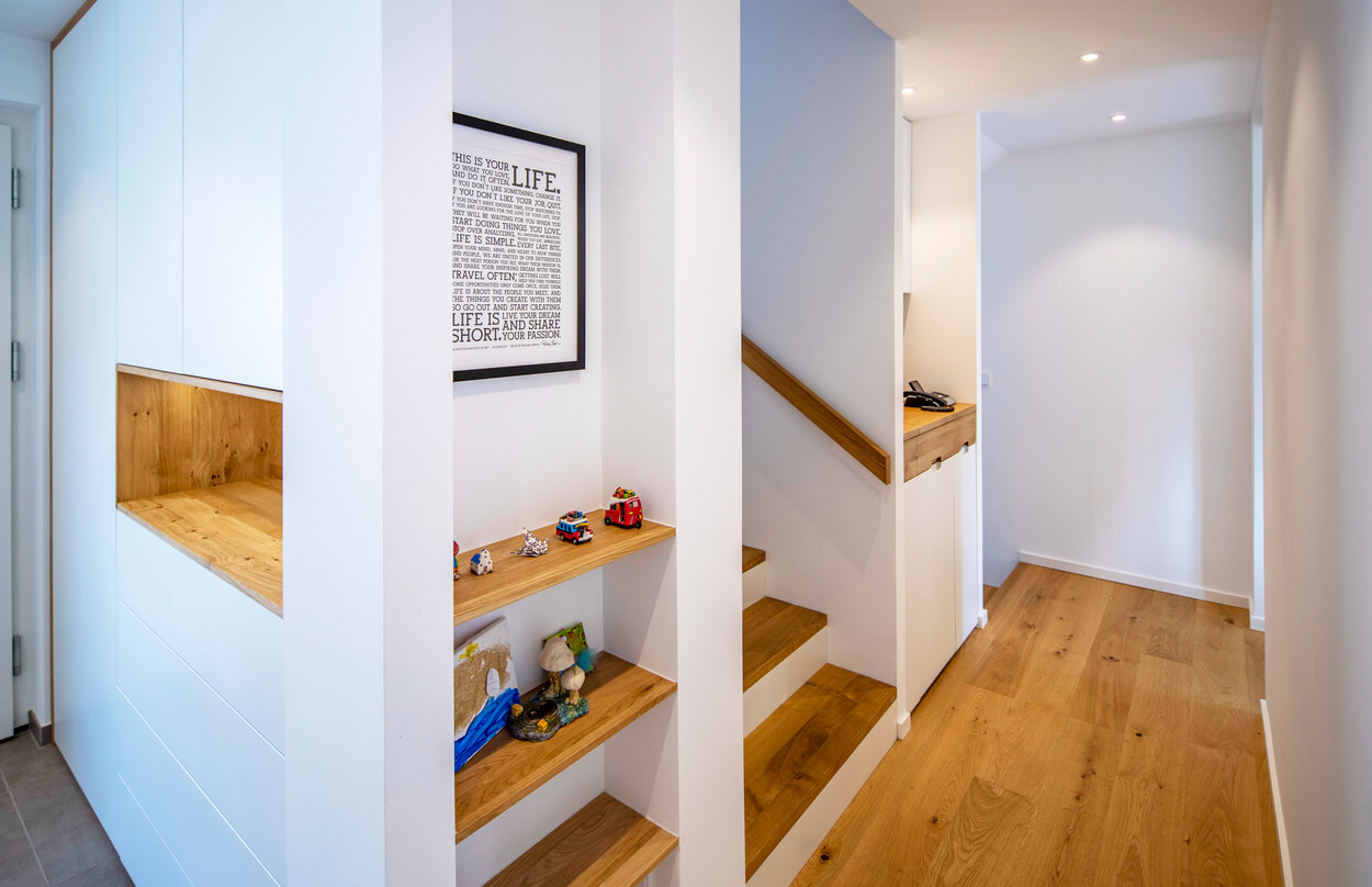 Ein moderner Flur im Passivhaus in Eichenau zeigt Holzregale, eine Treppe und dekorative Accessoires.