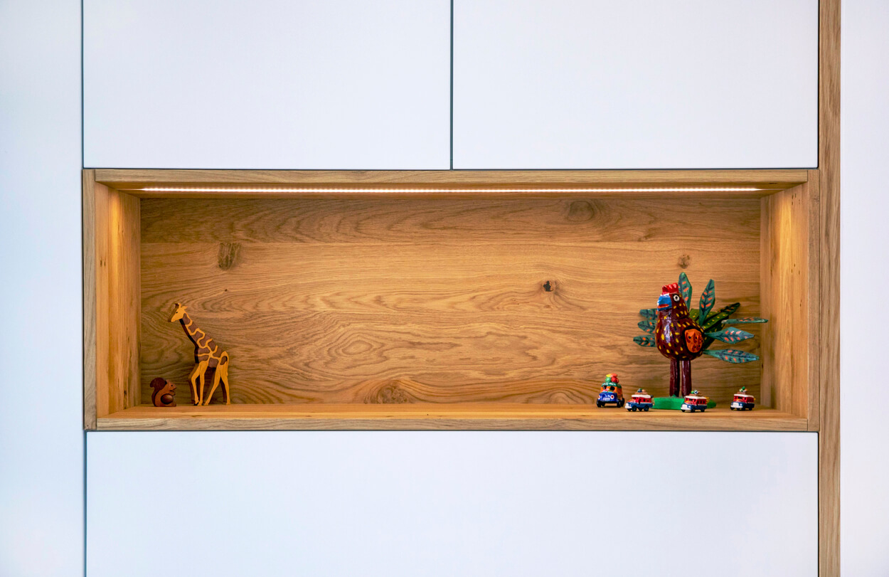 Ein minimalistisches Holzregal im Passivhaus-Stil in Eichenau präsentiert bunte Dekofiguren und Spielzeugautos.