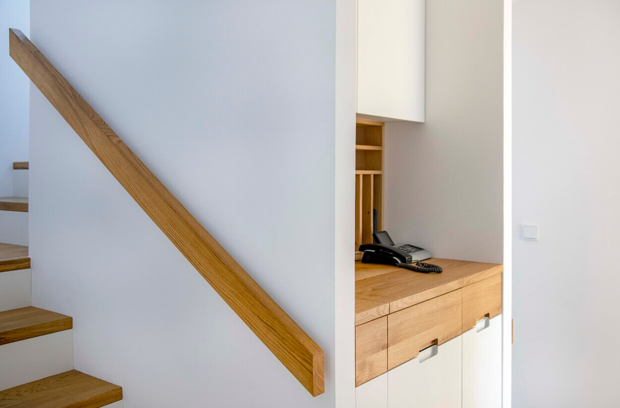 Ein modernes Treppenhaus in einem Passivhaus in Eichenau zeigt ein Holzgeländer und einen integrierten Telefonbereich.