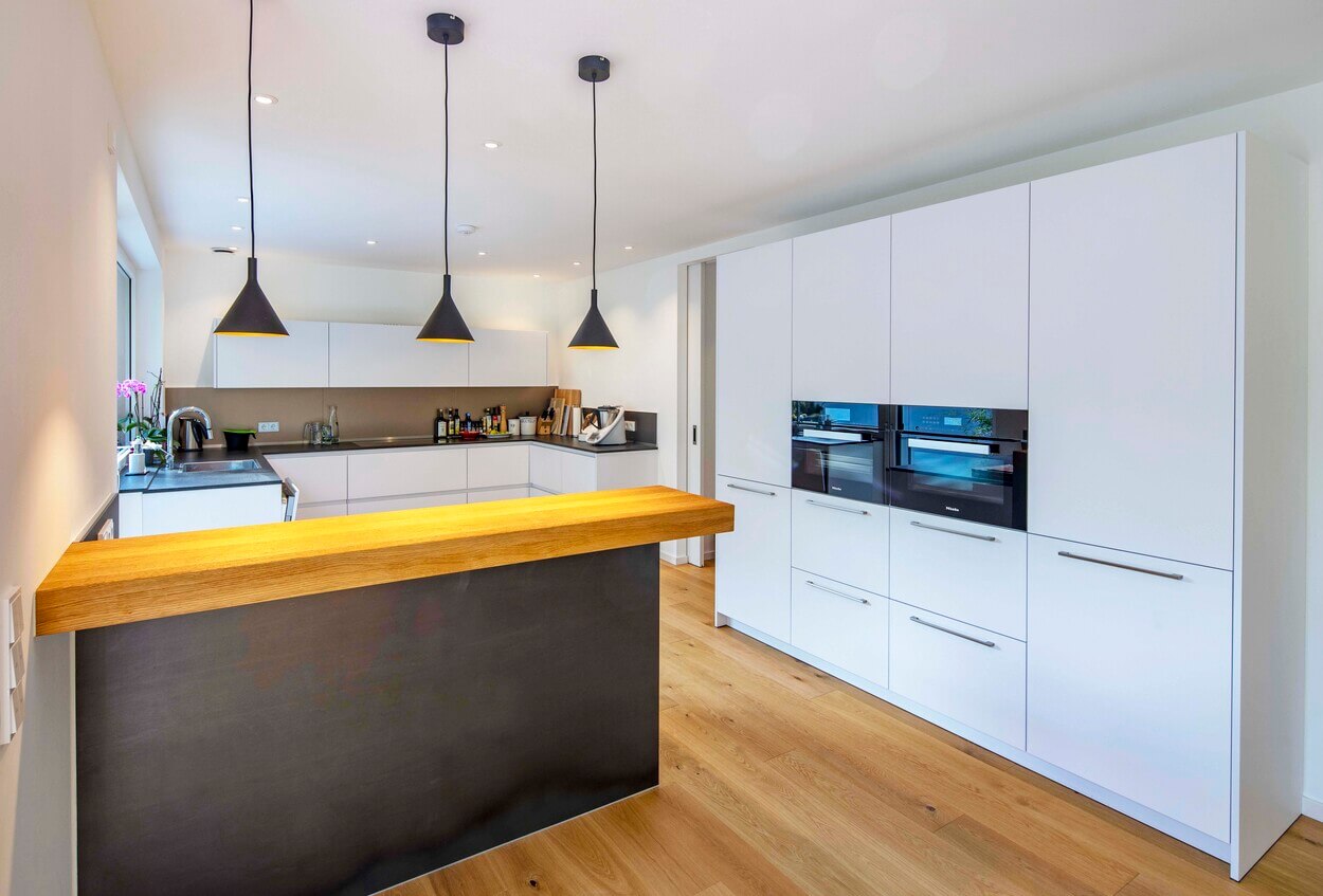 Moderner Wohnbereich im Passivhaus in Eichenau mit eleganter, weißer Küche und stilvoller Holztheke.