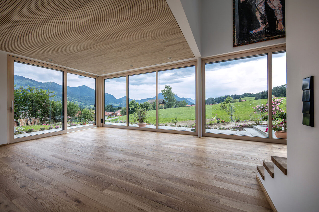 Große Fenster im Holzhaus am Samerberg bieten einen beeindruckenden Ausblick auf die grüne Landschaft und Berge.