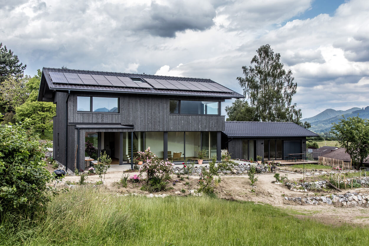Ein modernes Holzhaus mit großen Fenstern steht harmonisch in der grünen Landschaft von Samerberg unter einem bewölkten Himmel.