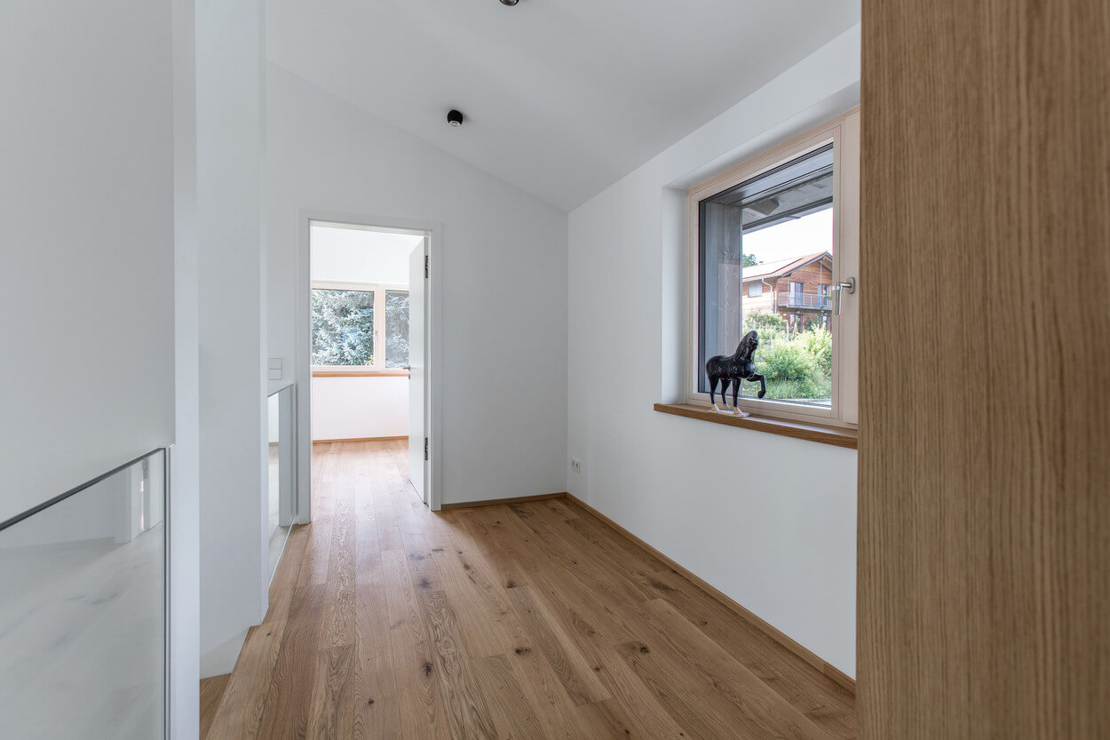 Ein heller Flur in einem Holzhaus zeigt einen Holzboden und ein Fenster mit Blick auf einen grünen Garten.
