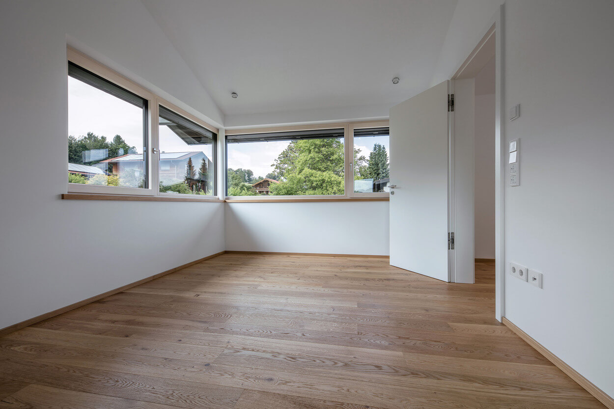 Ein helles Zimmer in einem Holzhaus in Samerberg zeigt durch große Fenster eine grüne Landschaft.