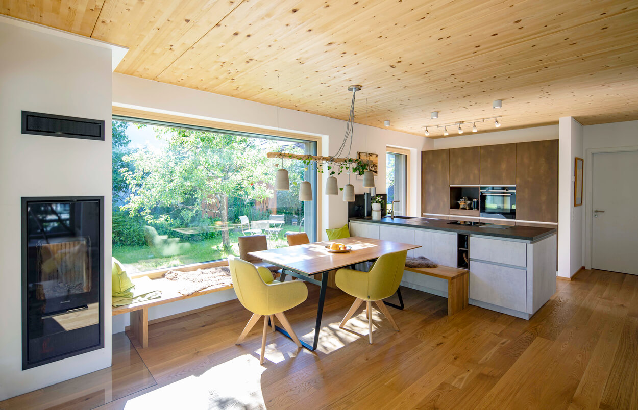 Ein modernes Esszimmer in einem Holzhaus in Otterfing mit gelben Stühlen bietet einen herrlichen Blick in den grünen Garten.