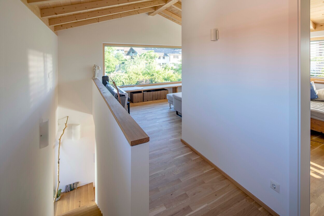 Ein Flur im Obergeschoss eines Holzhauses in Otterfing führt zu einem hellen Wohnbereich mit gemütlichem Ambiente.