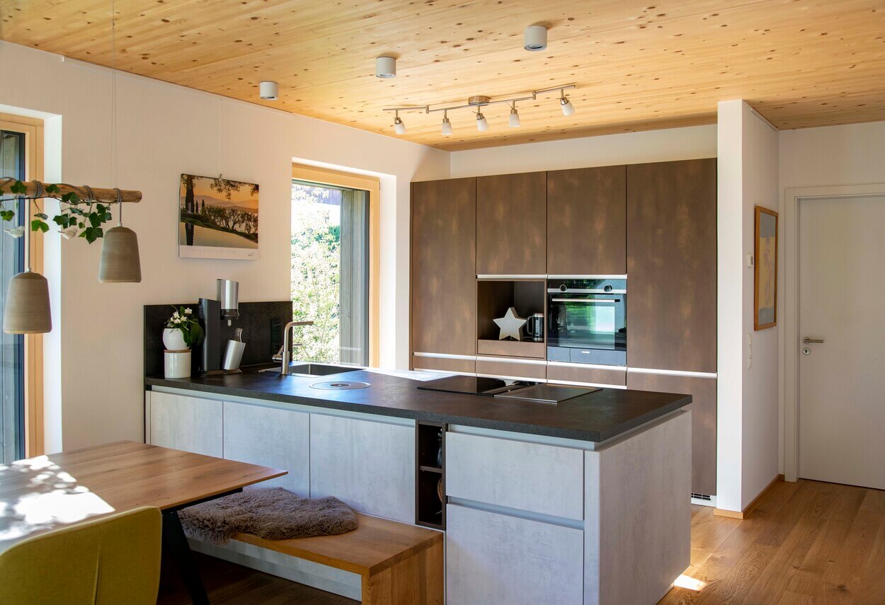 Moderne Küche in einem Otterfinger Holzhaus mit Holzdecke, zentraler Kochinsel und stilvoller Beleuchtung.