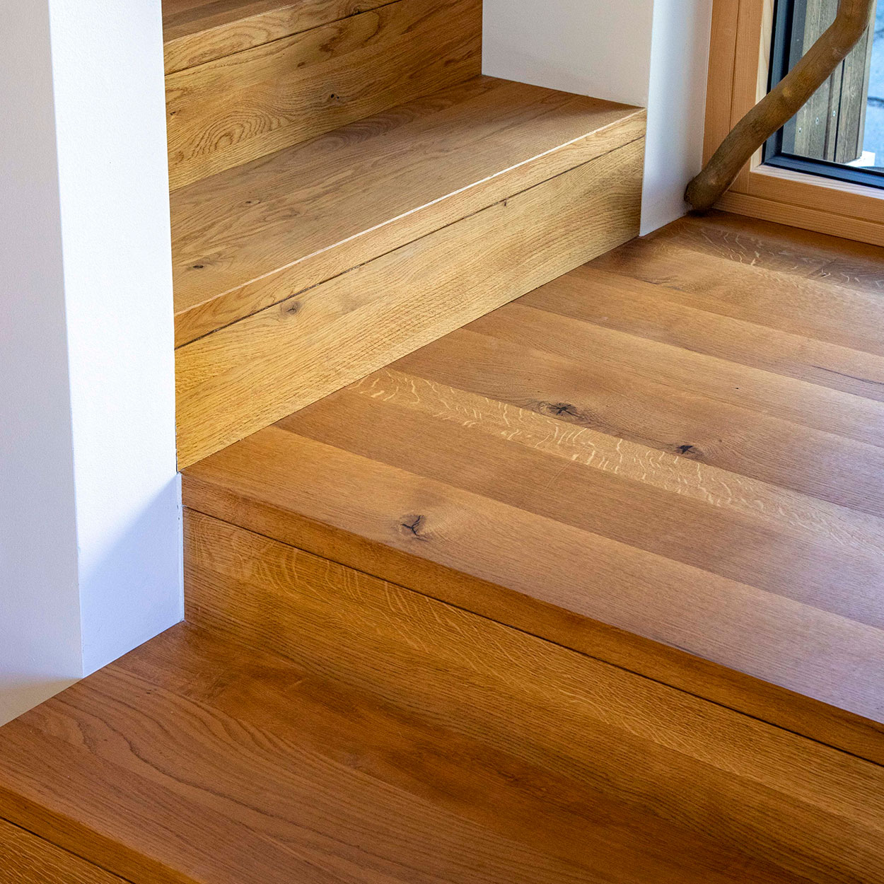 Detail einer Holztreppe in einem Haus in Otterfing, beleuchtet von natürlichem Licht durch ein angrenzendes Fenster.