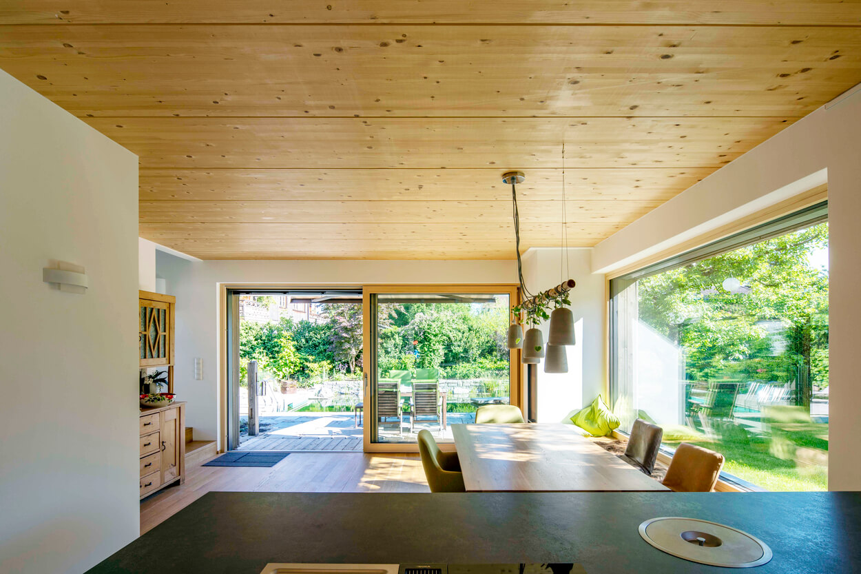 Der Wohnbereich eines Holzhauses in Otterfing bietet eine helle, moderne Einrichtung mit Blick auf den grünen Garten.