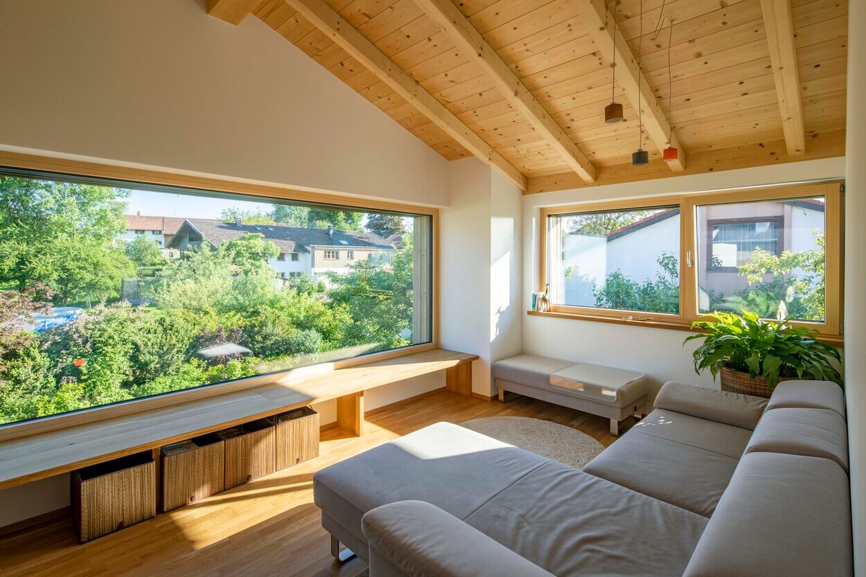 Ein gemütliches Wohnzimmer in einem Holzhaus in Otterfing bietet durch große Fenster einen malerischen Blick auf den grünen Garten.