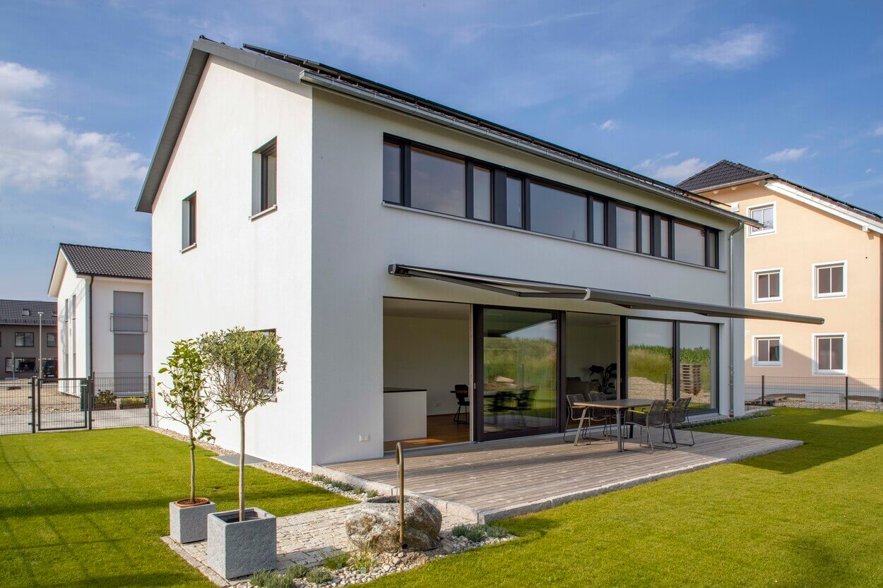Ein modernes Passivhaus in Pliening mit großzügiger Terrasse und gepflegtem Garten strahlt bei sonnigem Wetter.
