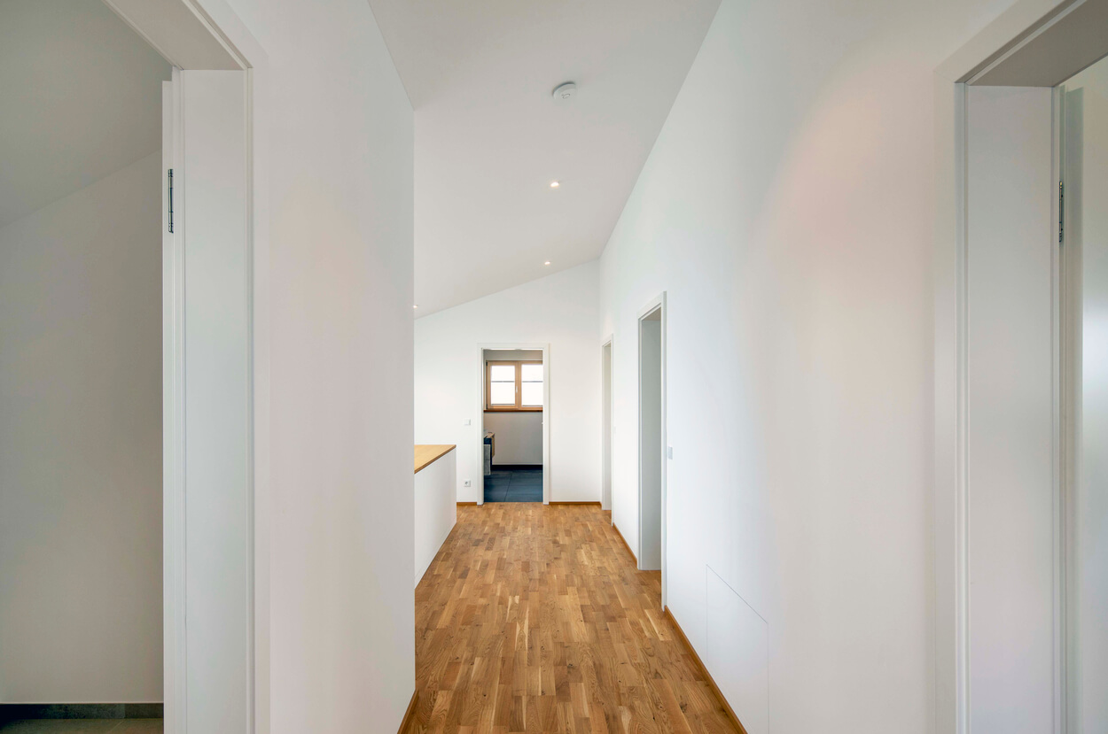 Ein heller Flur mit Holzfußboden im Passivhaus in Pliening führt zu mehreren geöffneten Türen.