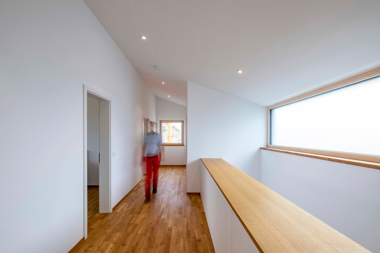 Ein Mann geht durch den hellen Flur eines Passivhauses in Pliening, das durch sein minimalistisches Design besticht.