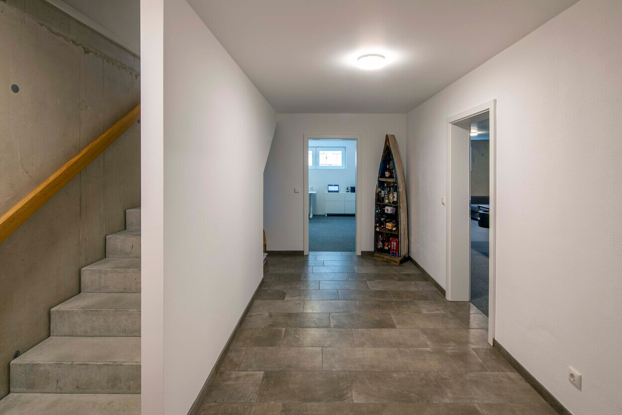 Ein heller Flur im Passivhaus Pliening führt links zur Treppe und rechts zu Räumen, geschmückt mit kreativen Dekorationen.