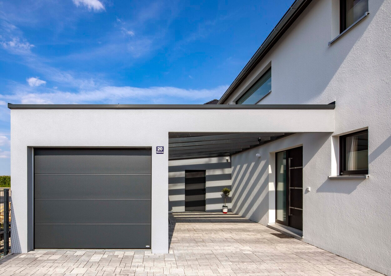 Ein modernes Passivhaus in Pliening mit klaren Linien und integrierter Garage wird von hellem Sonnenlicht beleuchtet.