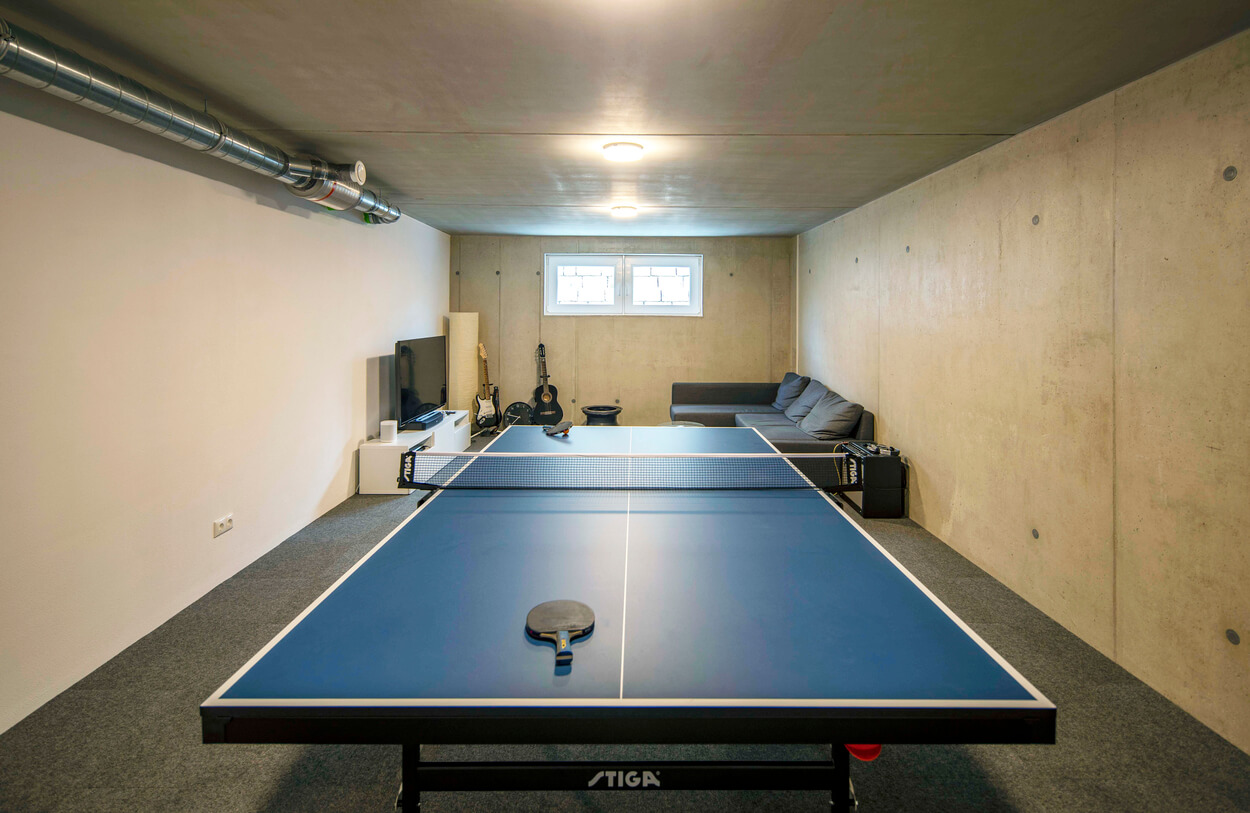 Ein moderner Hobbyraum im Passivhaus-Stil mit Tischtennisplatte, Sofaecke und Gitarren lädt zum Entspannen ein.