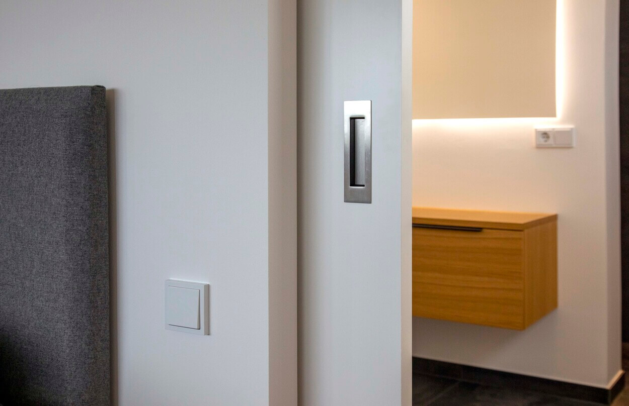 Eine elegante Schiebetür im Passivhaus Pliening öffnet den Blick auf ein stilvoll beleuchtetes, modernes Badezimmer.