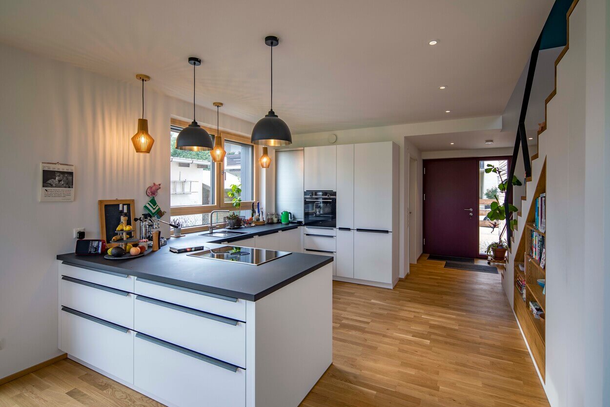 Moderne Küche in einem Holzhaus in Dachau mit weißen Schränken, Kochinsel und stilvollen hängenden Lampen.