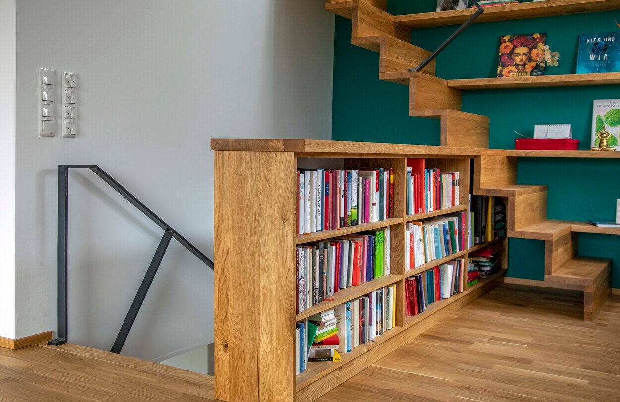 Eine moderne Holztreppe in einem Haus in Dachau integriert ein Bücherregal als funktionalen Stauraum.