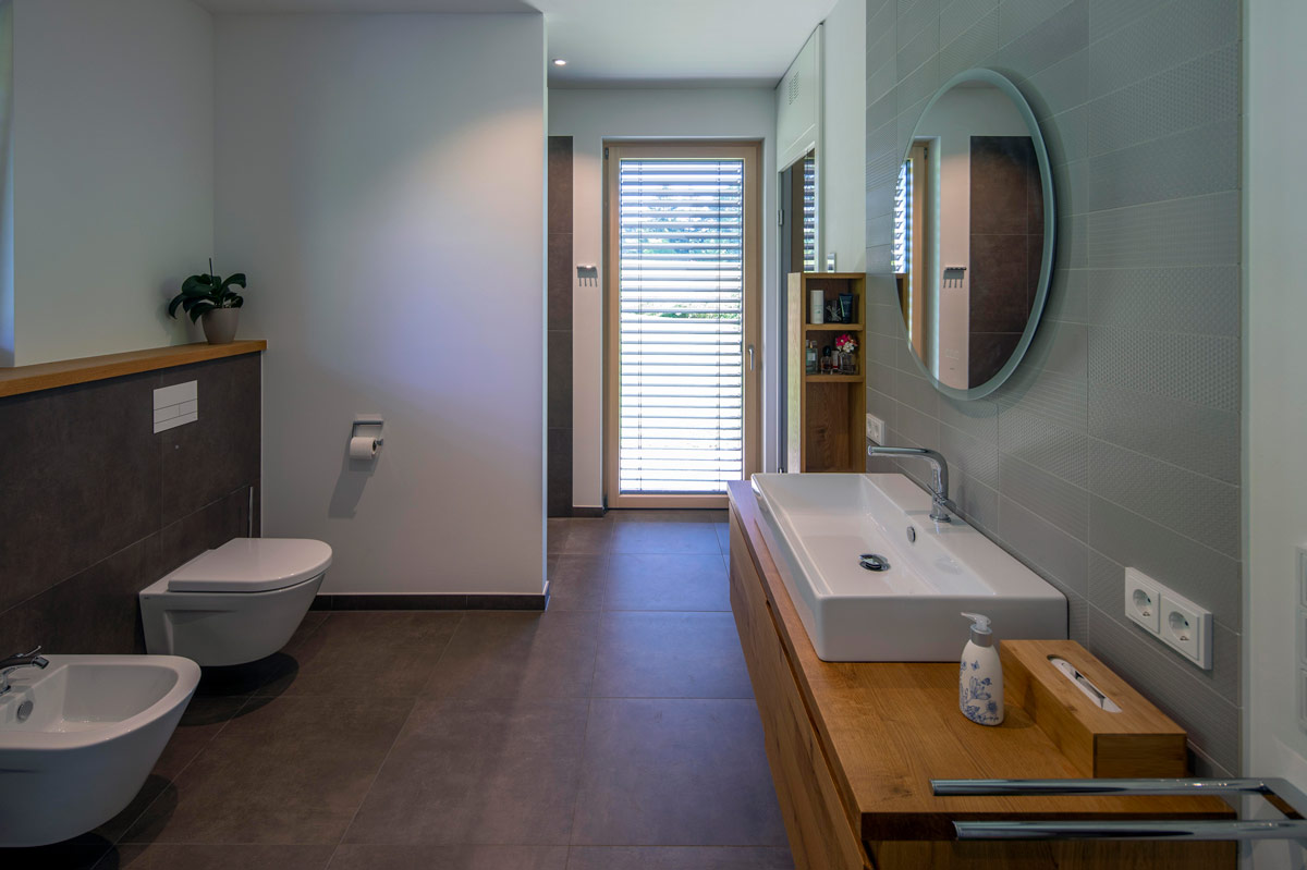 Ein modernes Badezimmer mit Holzdetails, einem großen Spiegel und einem Fenster, das reichlich natürliches Licht hereinlässt.