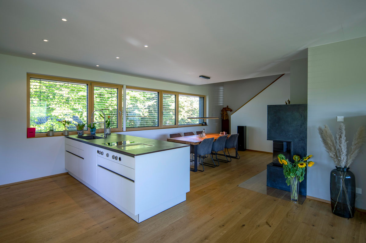 Moderne Küche in einem Holzhaus in Glonn mit großem Esstisch, hellen Fenstern und stilvoller Dekoration aus Blumen.