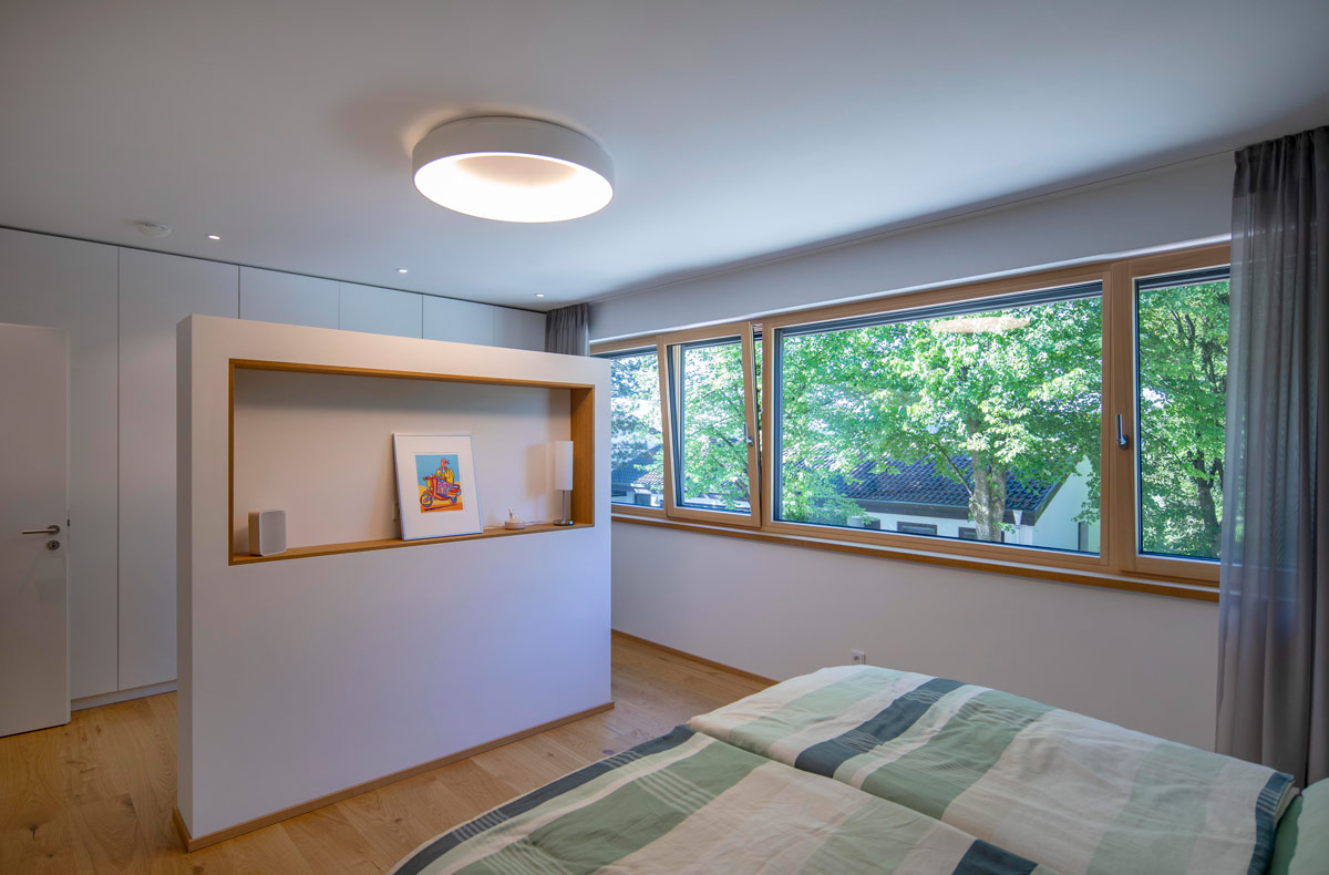 Ein modernes Schlafzimmer in einem Holzhaus in Glonn bietet durch große Fenster einen beeindruckenden Blick ins Grüne.